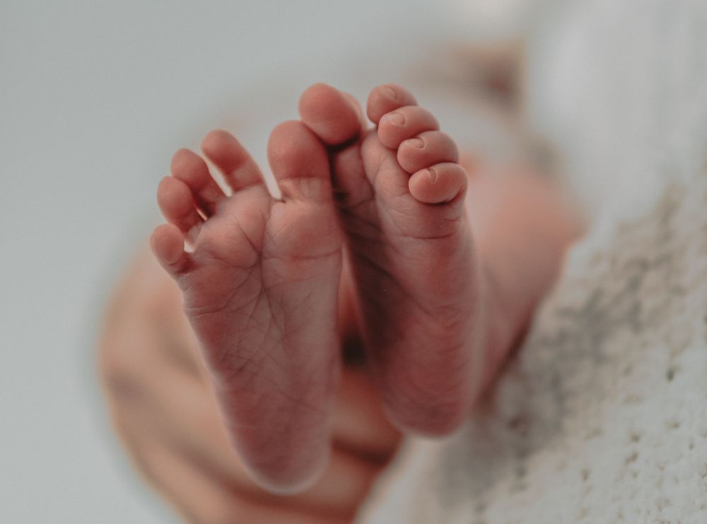 A little girls feet show adorably from below while behind held in her mother's arms.