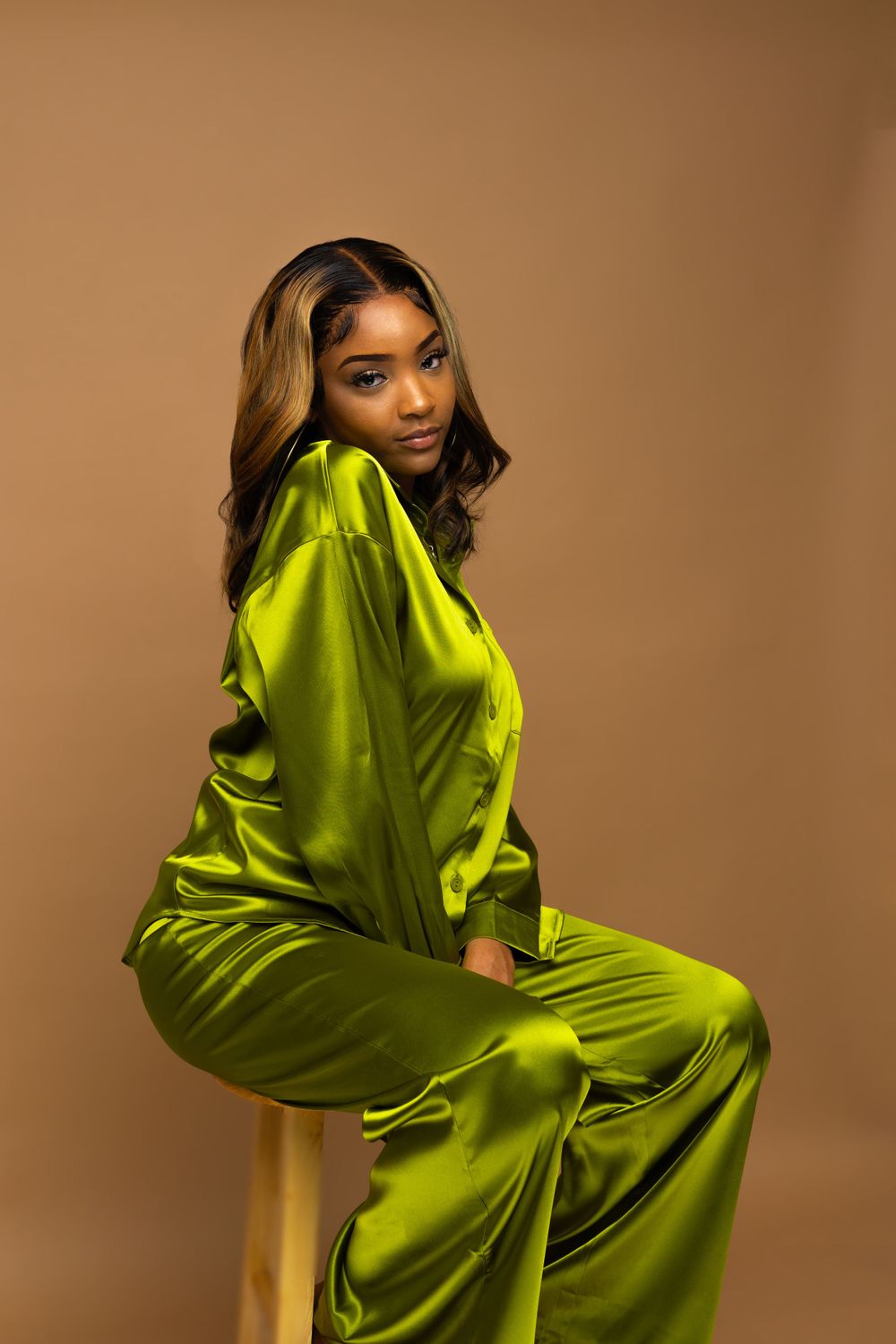 Fashion model poses in vibrant lime green silk pajama set against brown background.