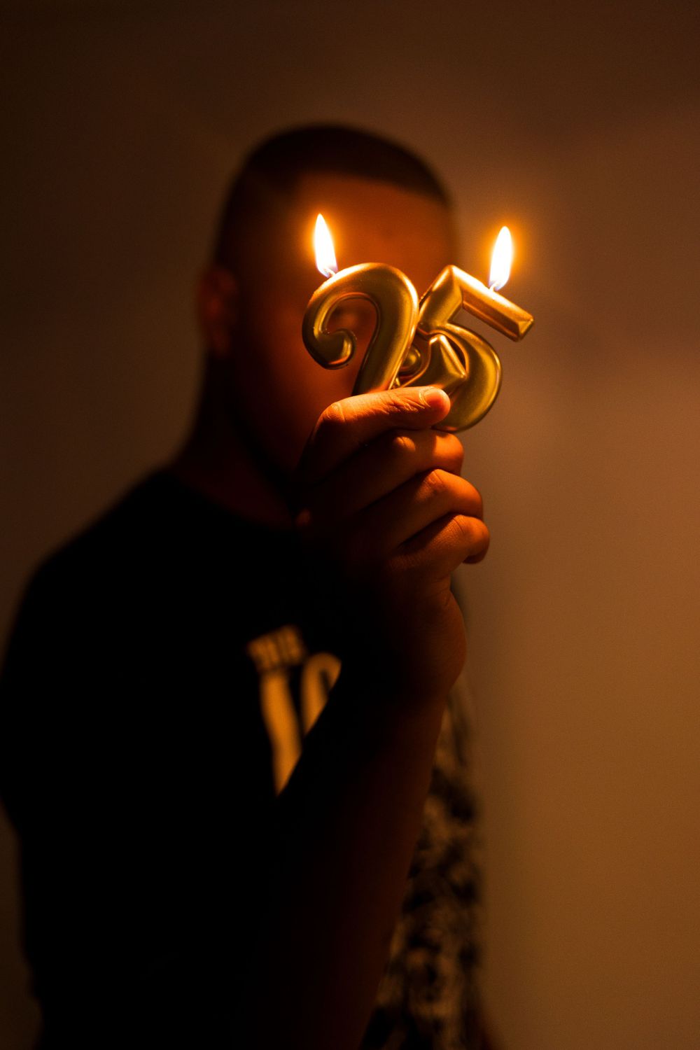 Artistic photo of a silhouetted figure holding illuminated number 25 candles in the darkness.