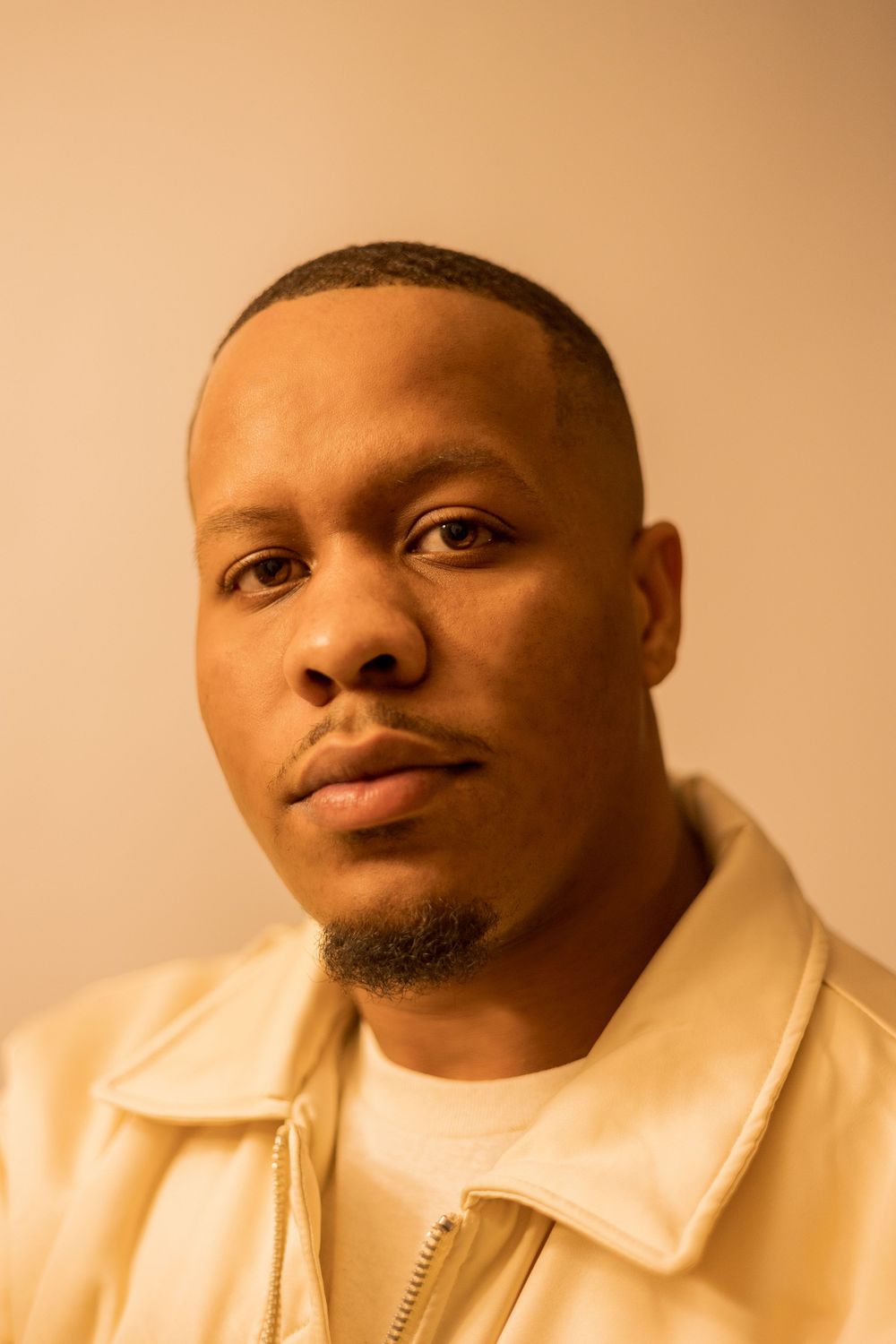 Close-up portrait of a person wearing a cream jacket against a warm-toned background.