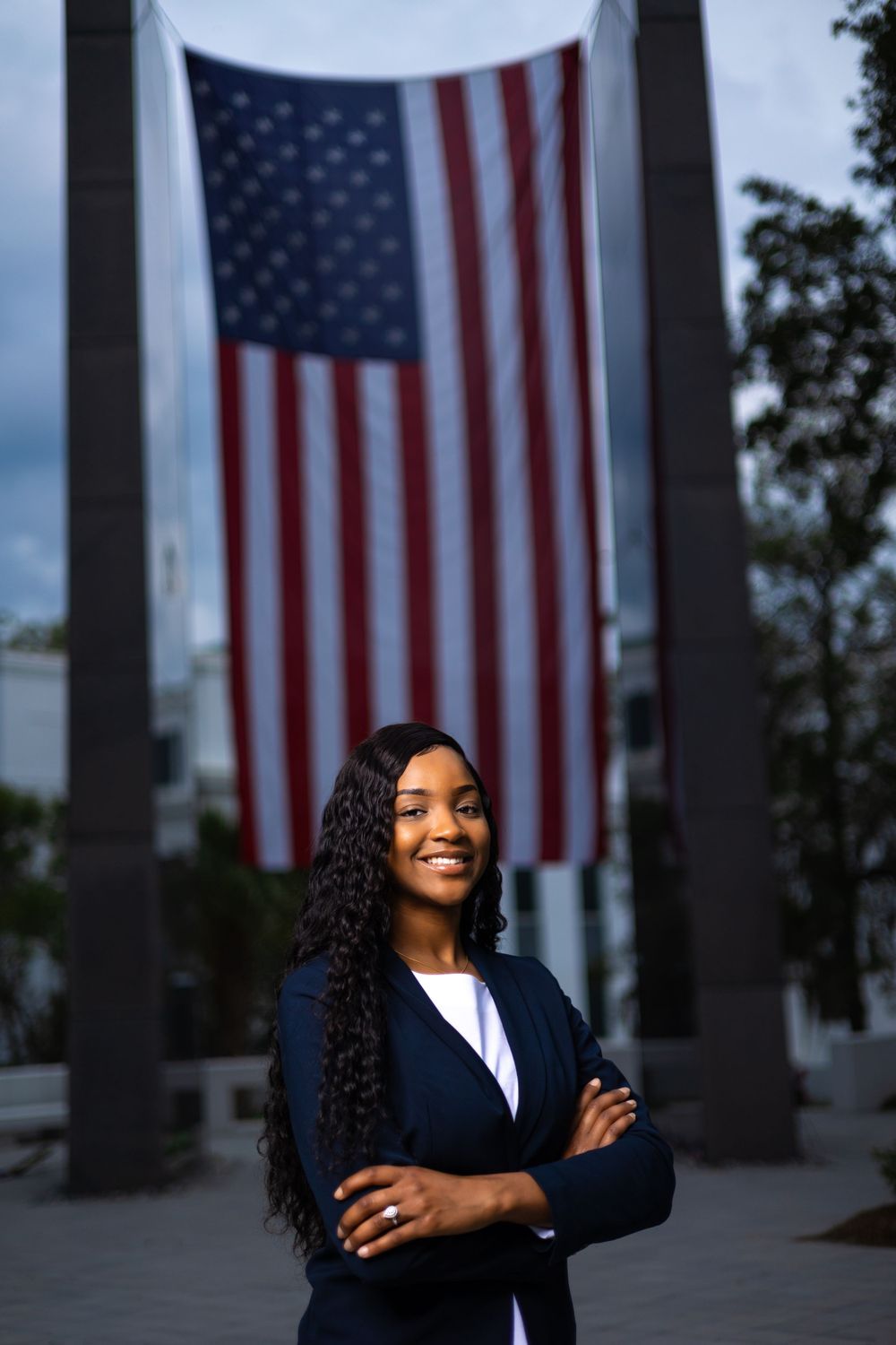 A professional in business attire poses confidently in front of a large American flag display.
