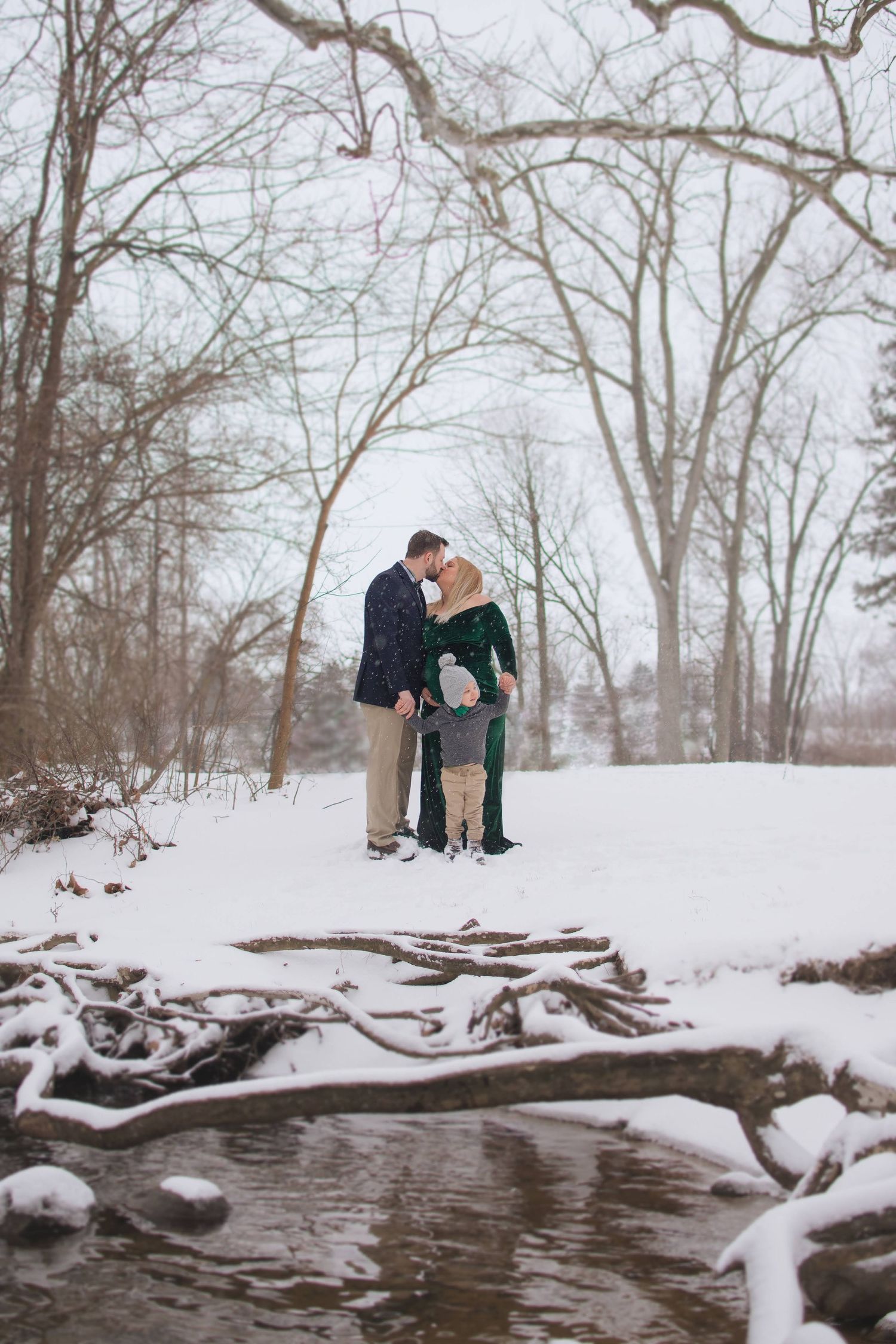 Pregnant woman surrounded by snow, sharing a tender moment with her toddler and husband. Heartwarming family photography