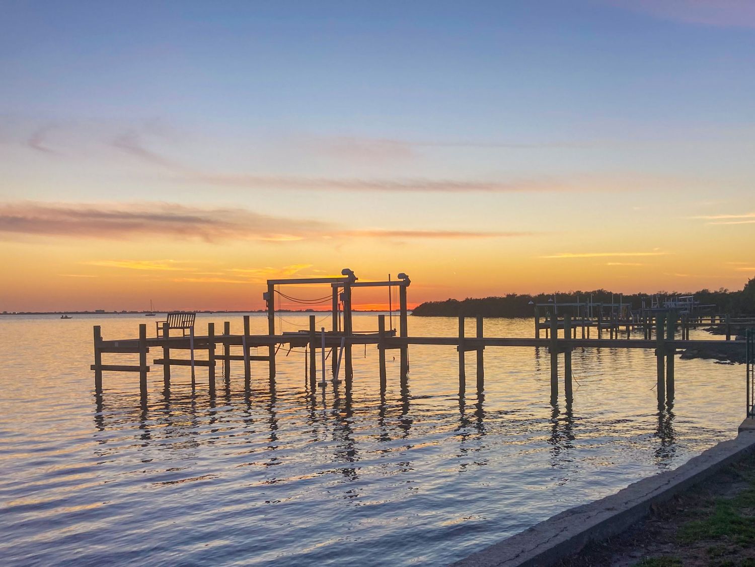 Wooden pier and boat lift silhouetted against vibrant orange sunset over calm waters.