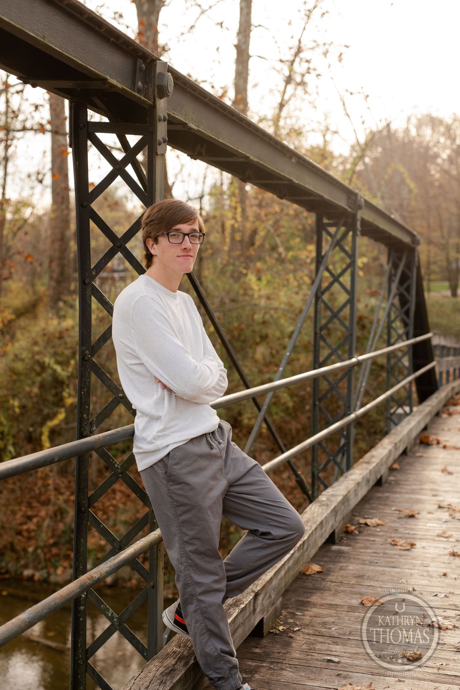 A person leans against railings on an old metal bridge during autumn.