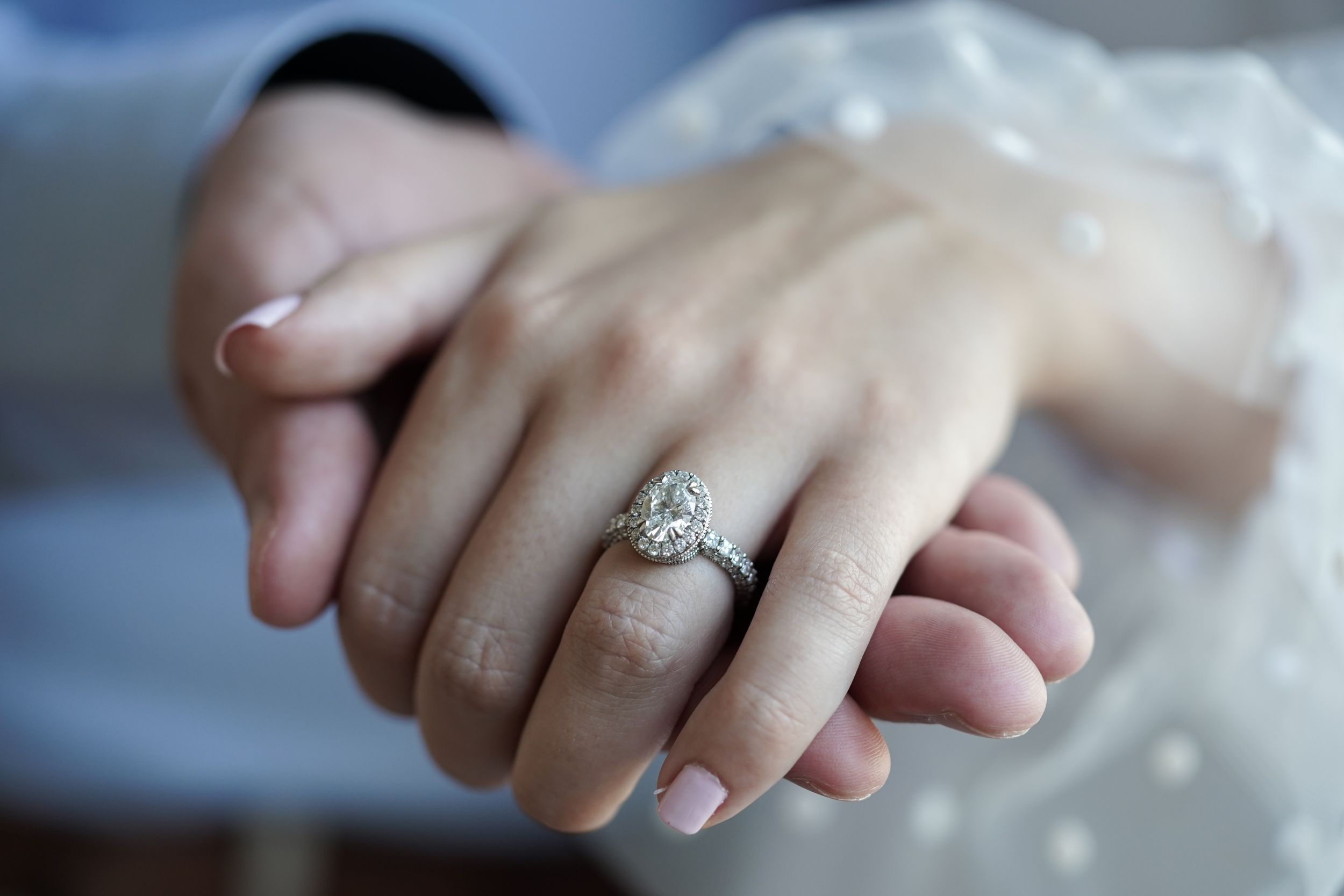 Close-up of an elegant oval diamond halo engagement ring on a bride's hand.