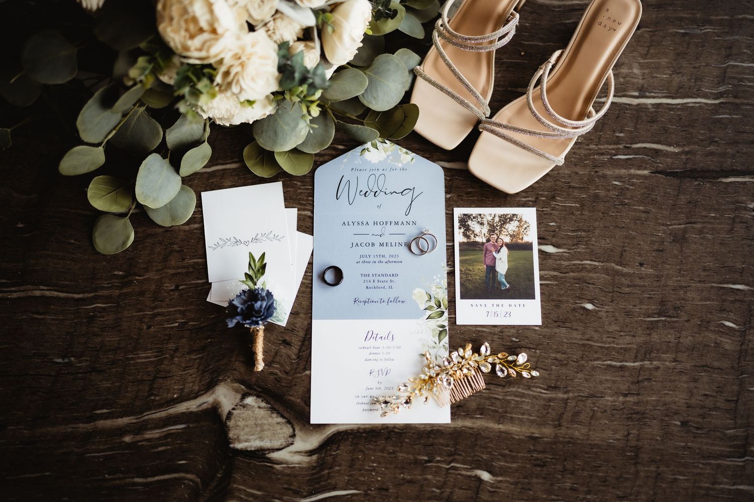 Wedding invitation suite with eucalyptus leaves, beige heels, and floral details on dark wooden surface.