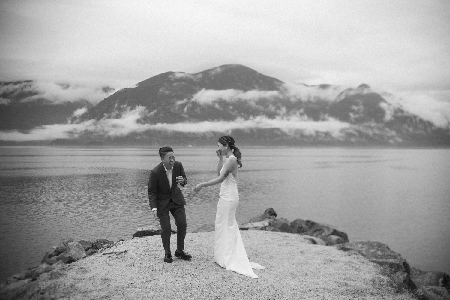 Couple shares an intimate moment on a rocky outcrop overlooking misty mountain landscape.