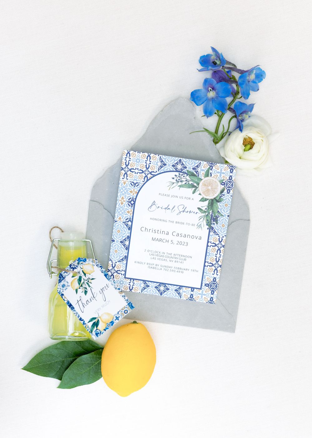 Wedding invitation with blue floral design styled with lemon, flowers and drink.