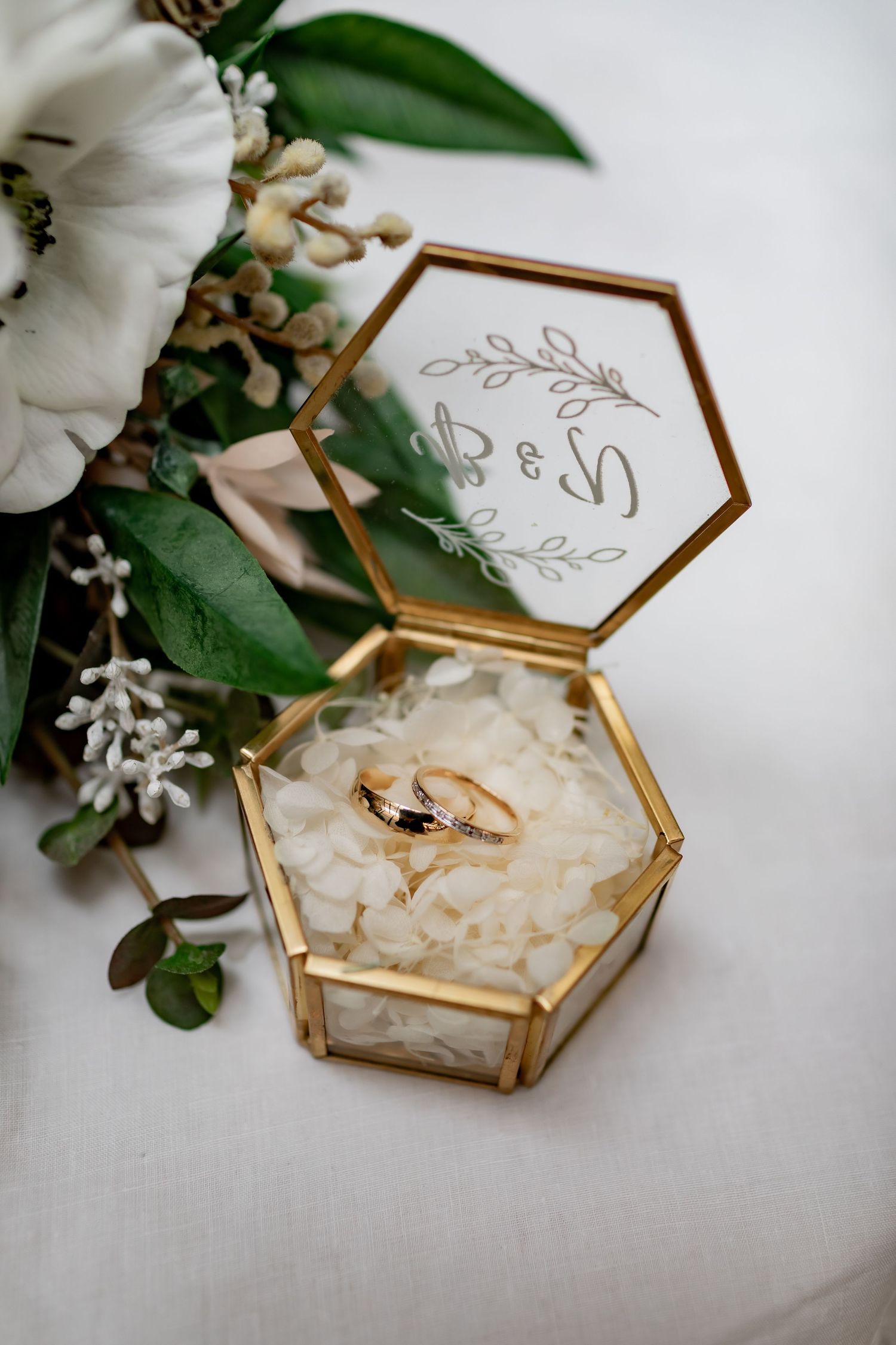 Gold hexagonal ring box with wedding bands nestled among white floral decor.