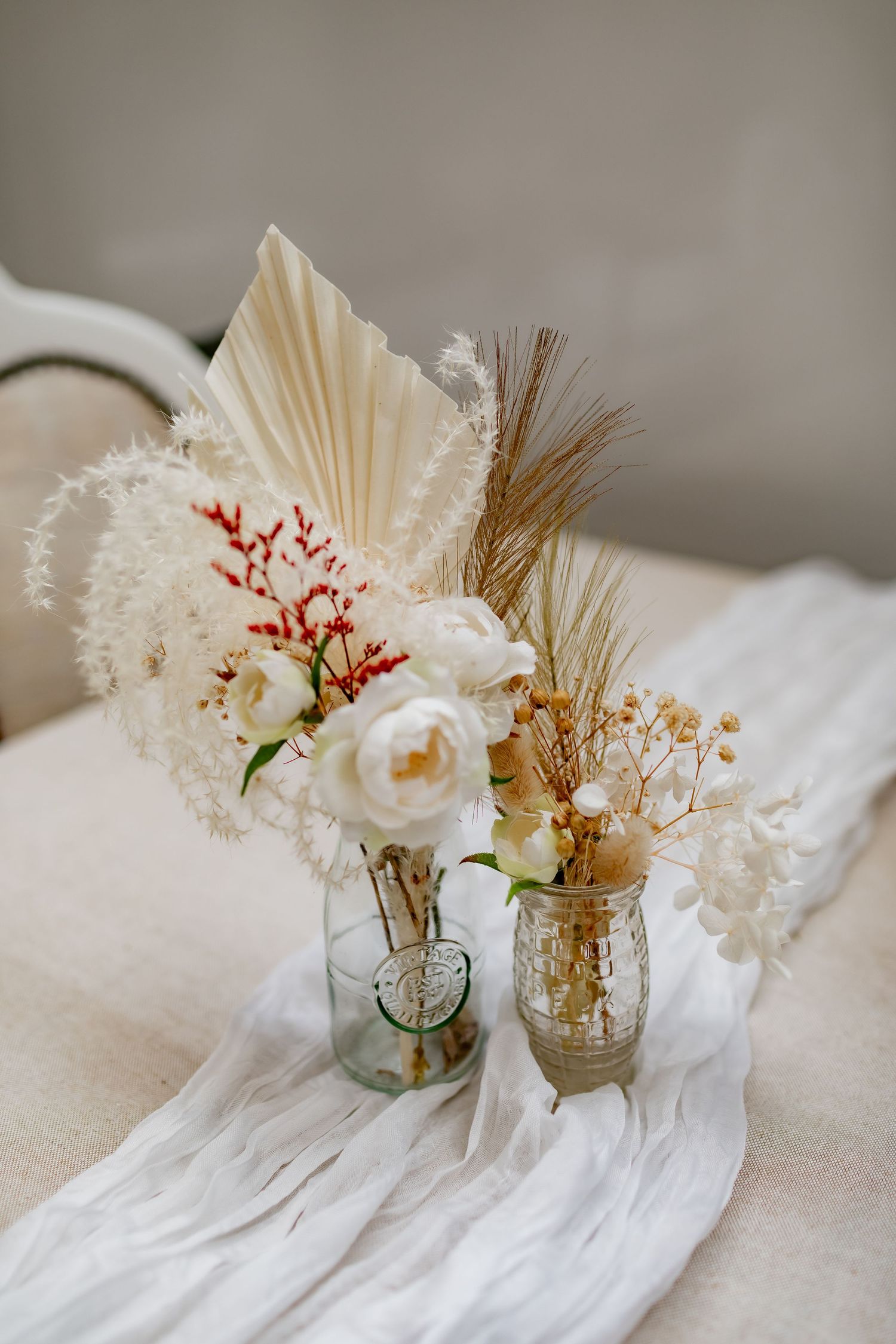Vintage-inspired floral arrangement with white flowers and dried elements in glass jars.