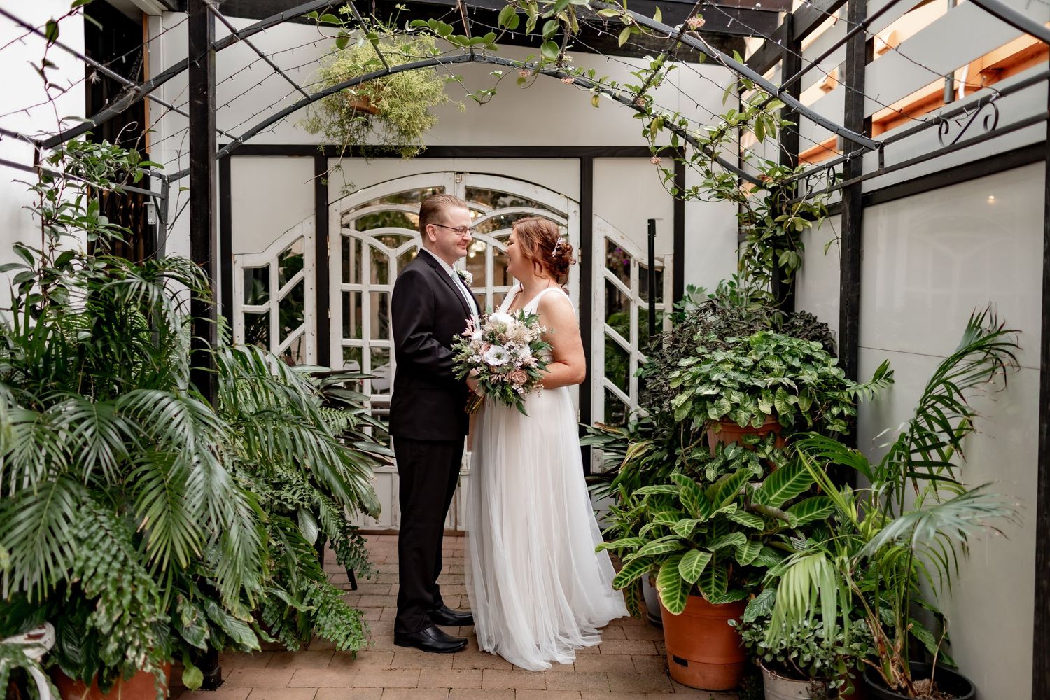 Wedding ceremony under arch decorated with greenery and white flowers.