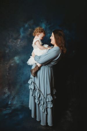 Mother and child in matching gray and white outfits embrace against dark studio backdrop.