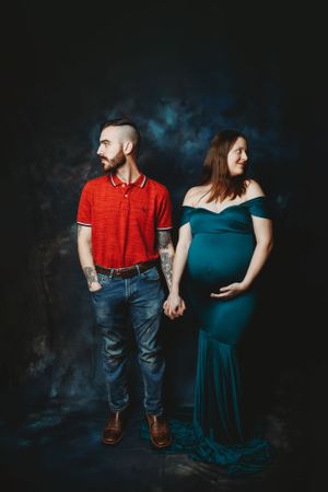 Couple in casual attire posing together during maternity session with moody lighting.