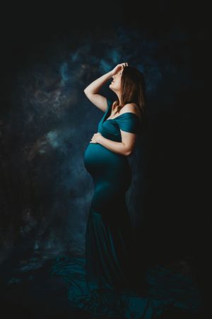 Silhouette of person in teal dress against dramatic blue-toned studio background.
