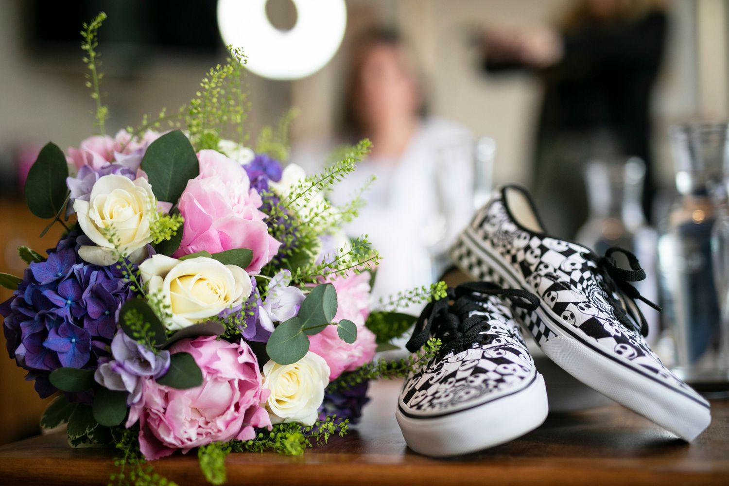 Wedding detail shot of pink and purple floral arrangements with white sneakers in the background.