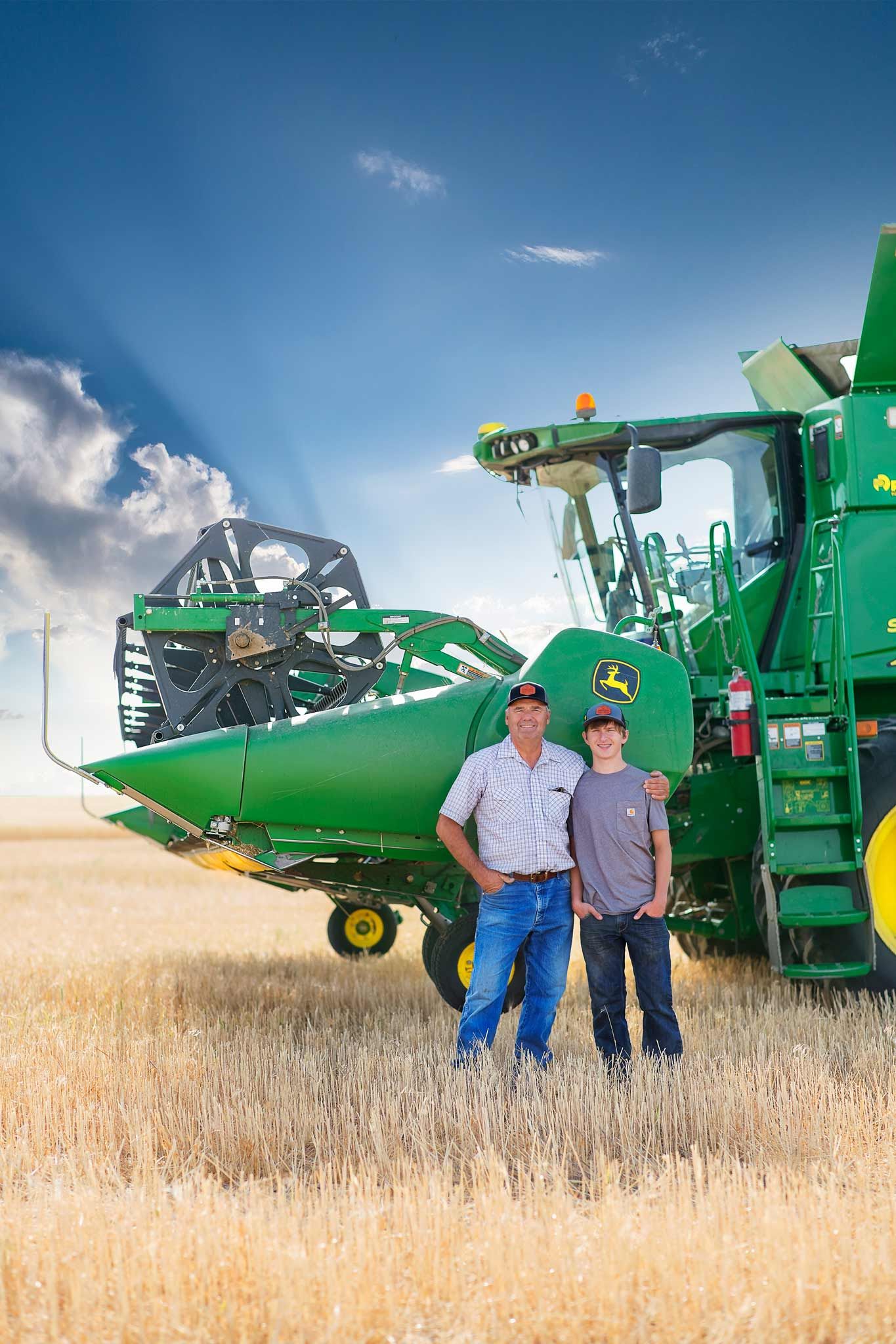 grandfather and grandson standing by wheat combine in field at harvest
