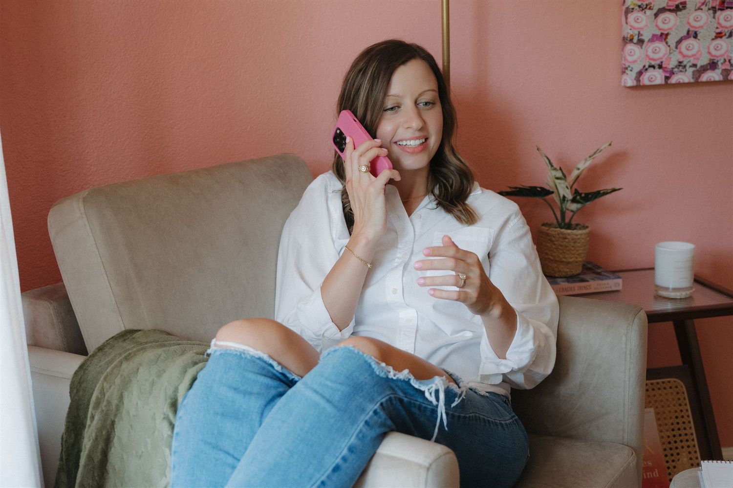 Someone in casual attire talking on pink phone while relaxing on beige couch.