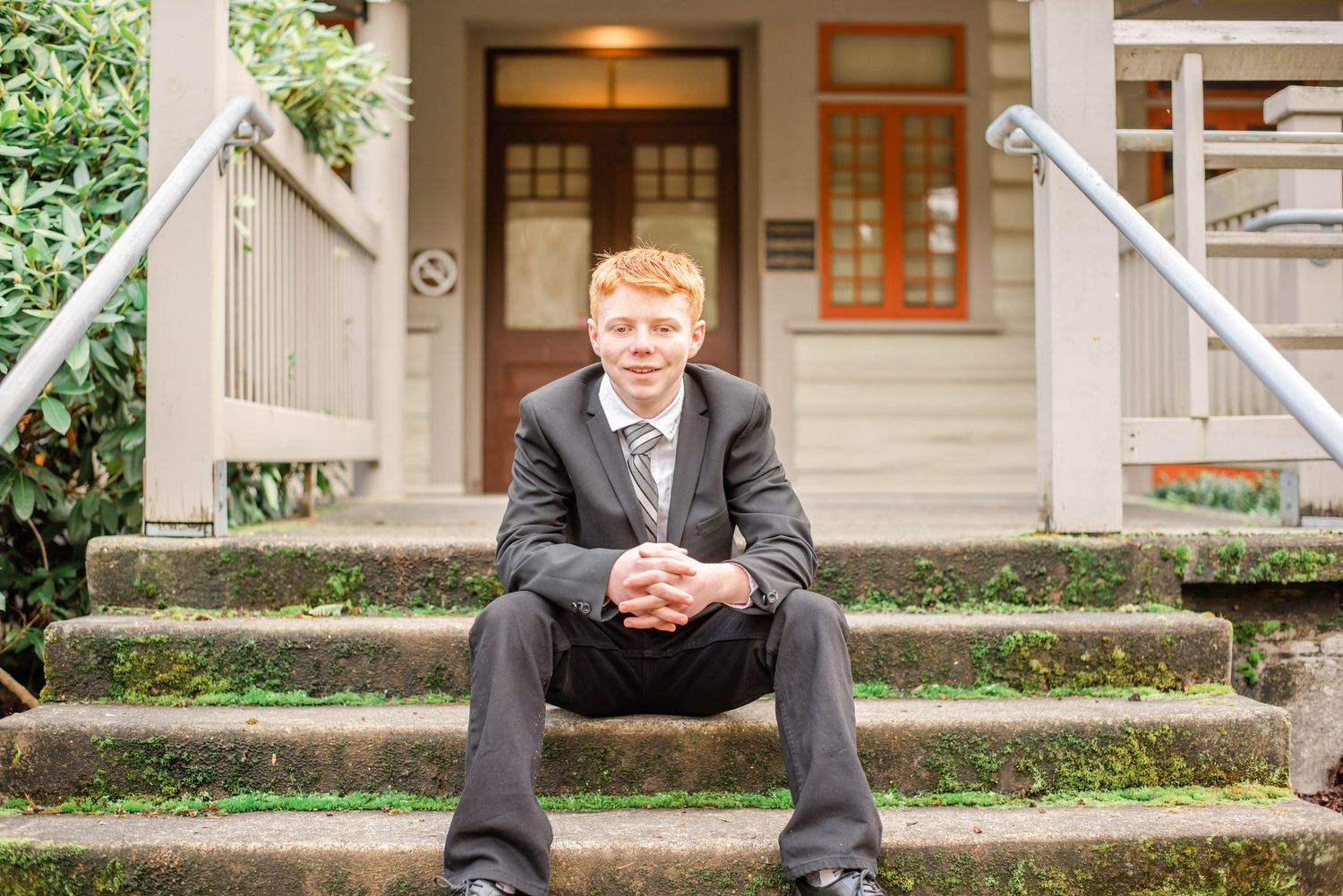 A formal portrait session outdoors with brick steps and white columns frames a subject in a black suit.