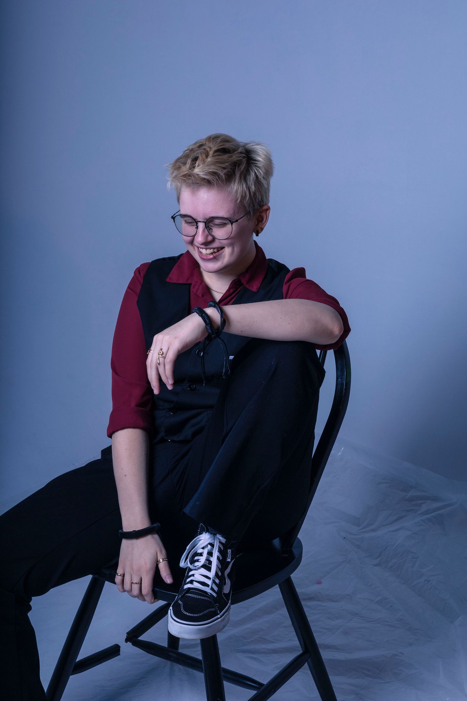 Person in burgundy shirt sitting casually on black chair against blue background.