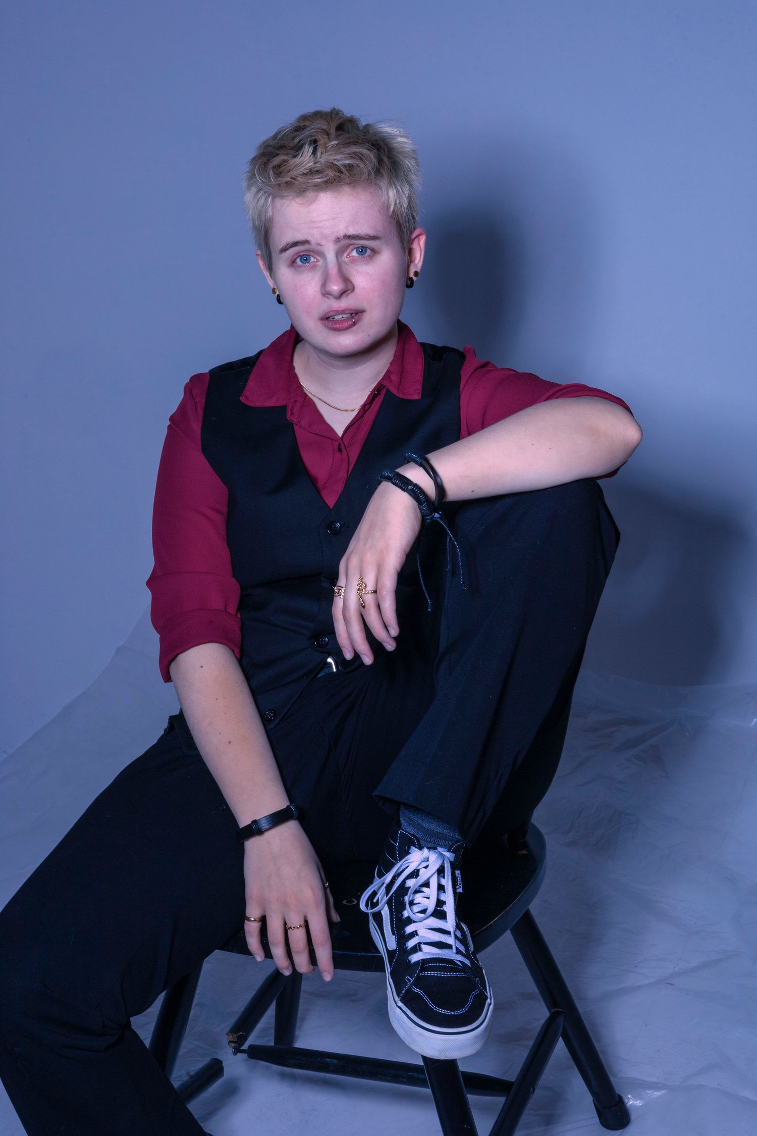 Youth in casual attire posed on black chair against blue studio backdrop.