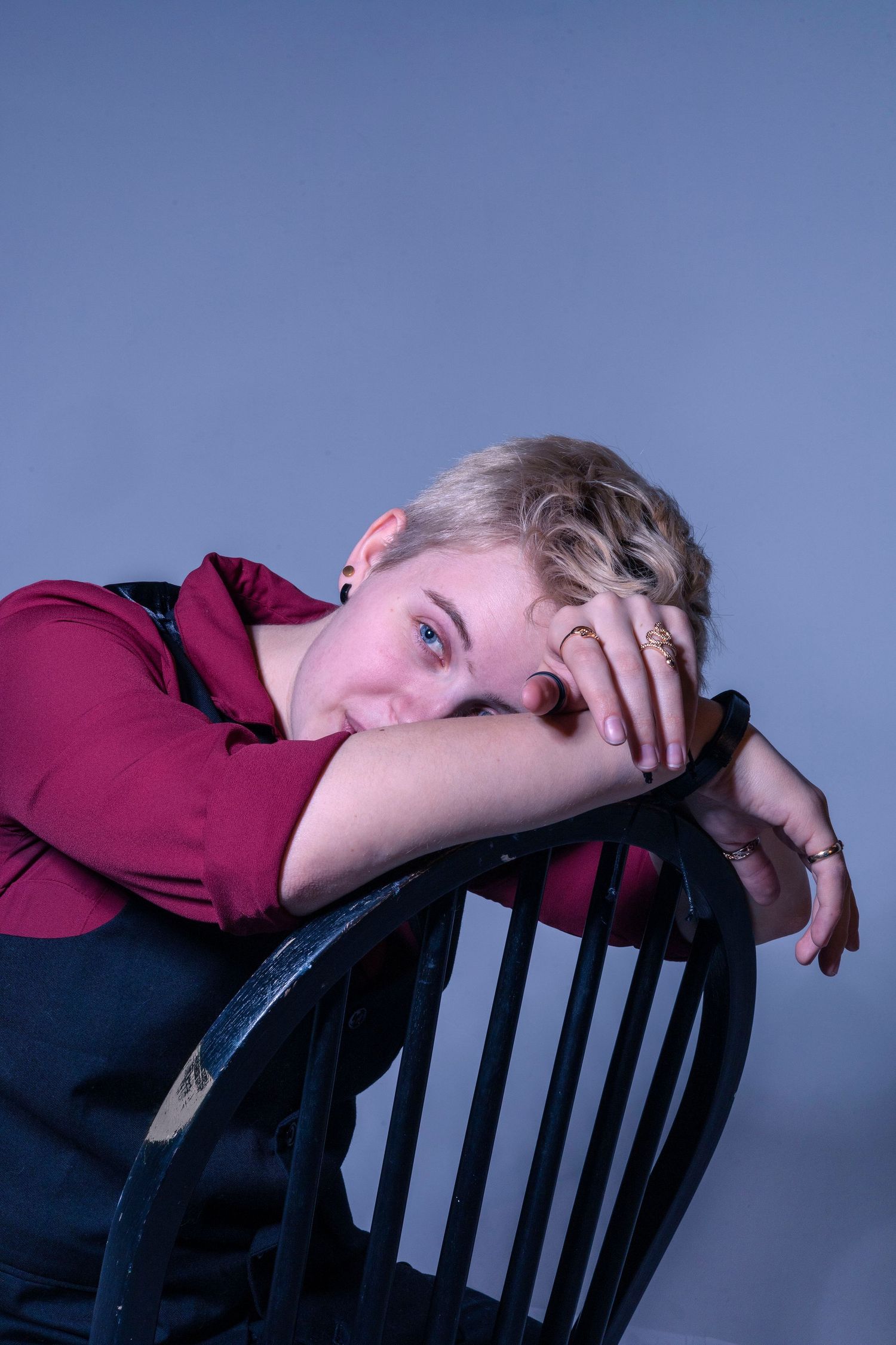 Person in burgundy shirt resting head on black chair in moody lighting.