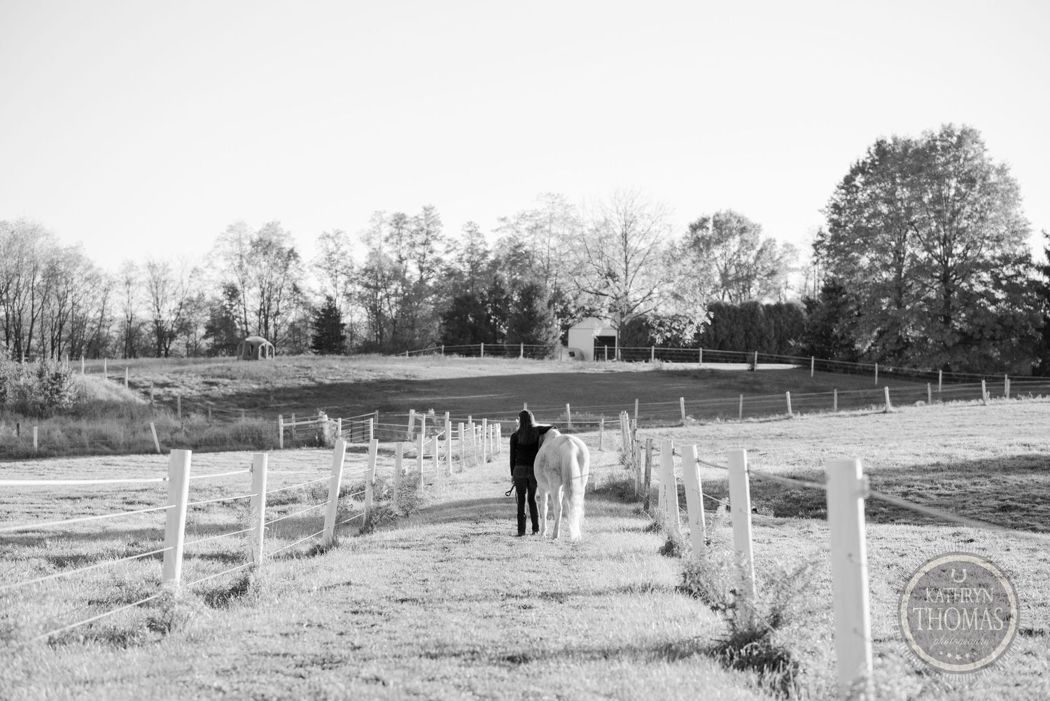 Black and white photo of person walking with horse between fence posts.