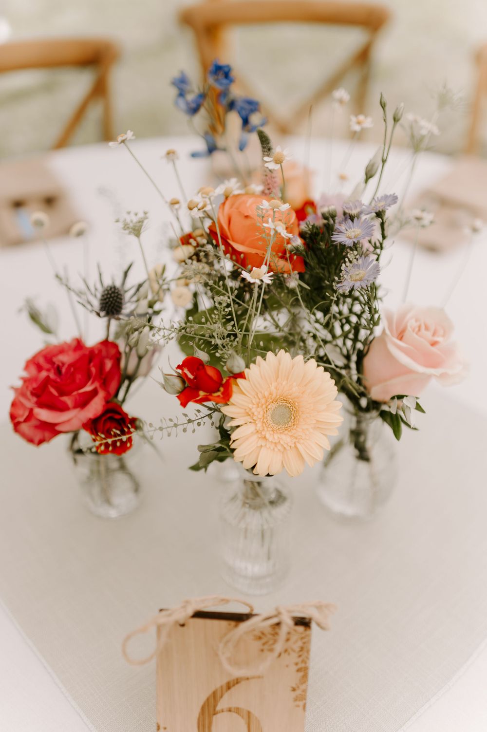 Colorful floral centerpieces with roses and daisies on white tablecloths.