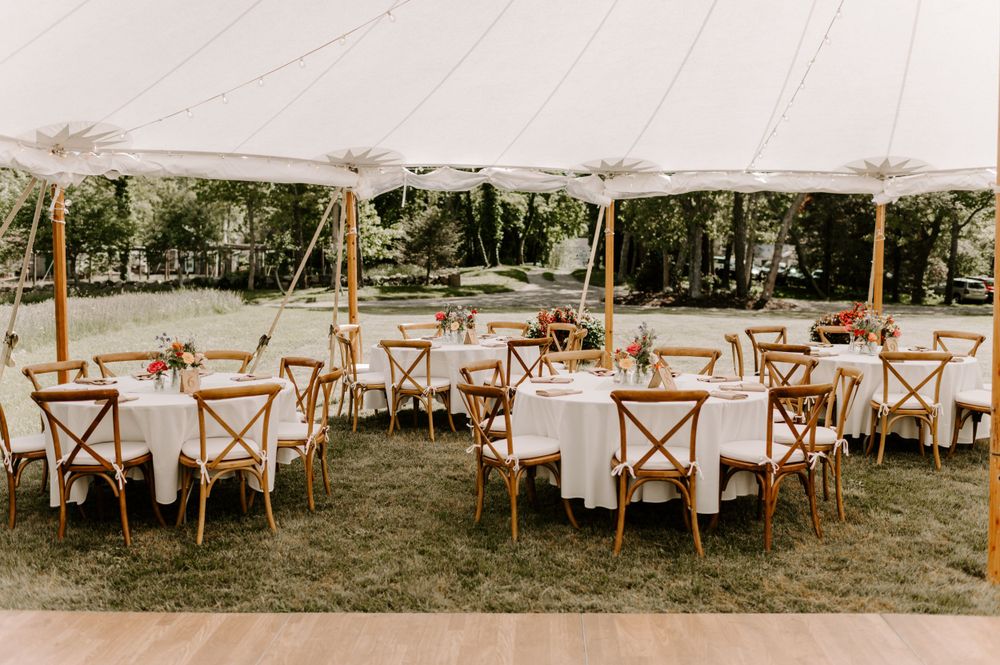 Panoramic view of an outdoor wedding reception setup with white tents and wooden chairs.