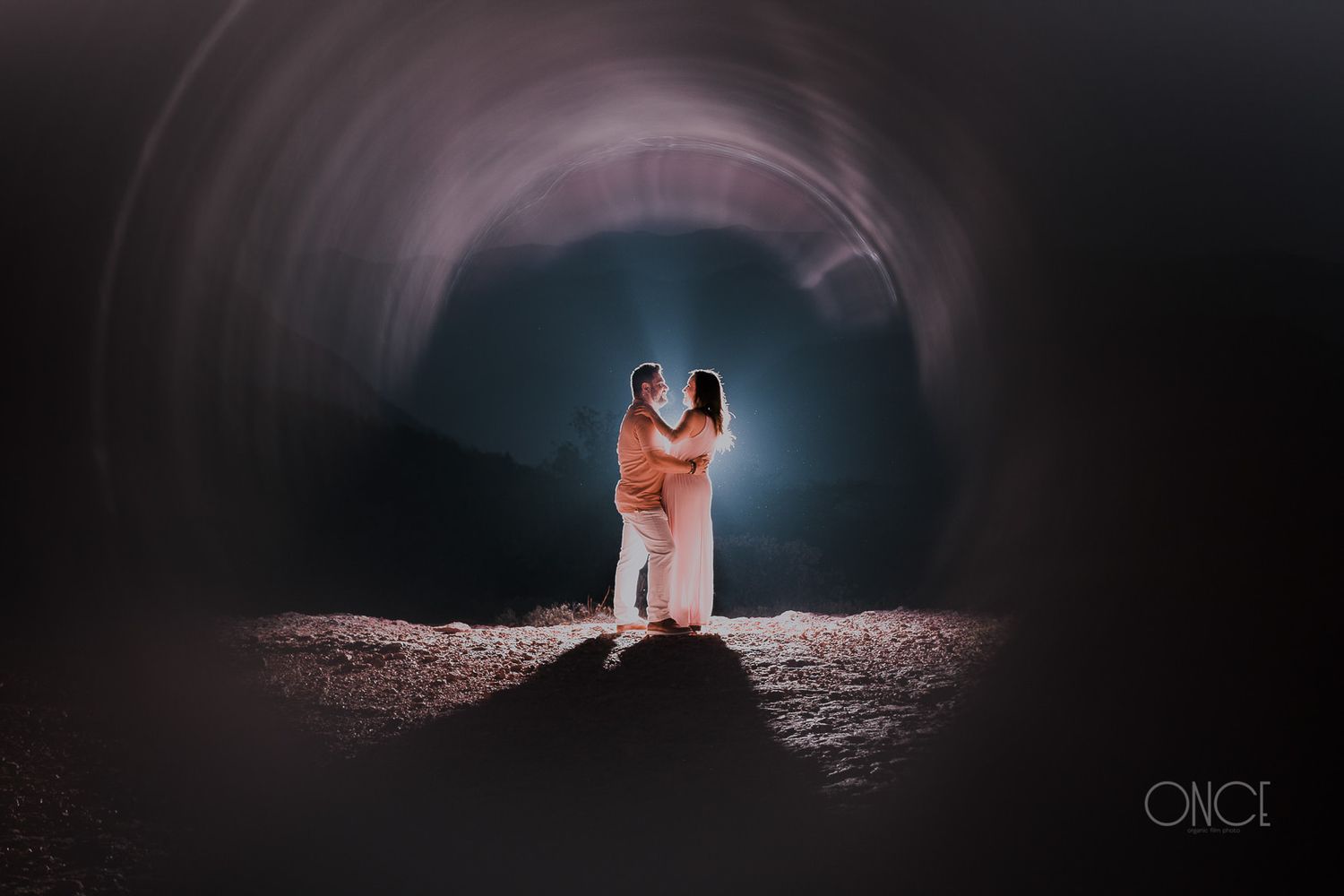 A romantic couple embracing in a dimly lit tunnel with dramatic lighting effects.