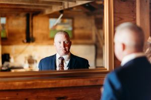 Groom checks his appearance in mirror before wedding ceremony in rustic venue.