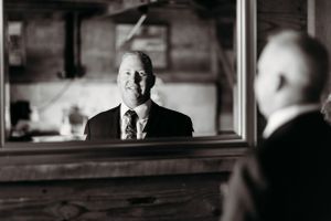 A black and white reflection of a person in formal attire looking in a mirror.