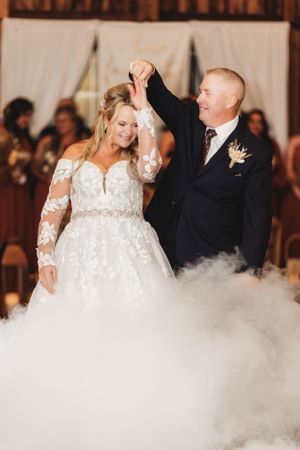 Newlyweds share their first dance surrounded by fog effects on wooden dance floor.