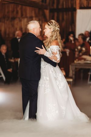 Couple shares intimate dance moment surrounded by atmospheric fog in rustic barn setting.