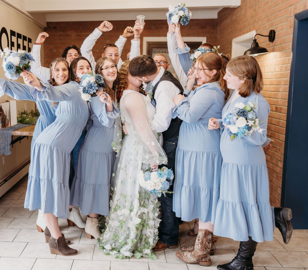 Wedding party celebrating with bride in flowing dress and bridesmaids in light blue dresses.
