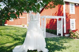 A pristine white wedding gown displayed against a red barn in natural sunlight.