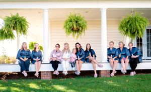 Wedding party members seated on white porch with hanging ferns and blue attire.