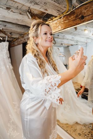 Getting ready scene in bridal suite with wedding dresses visible in background.