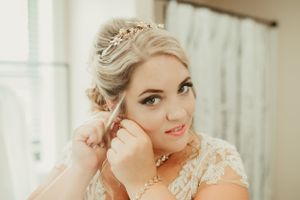 Close-up of bride putting on earrings during wedding preparation.