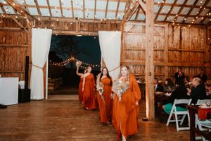 Wedding party in bright orange dresses performs during rustic barn reception.