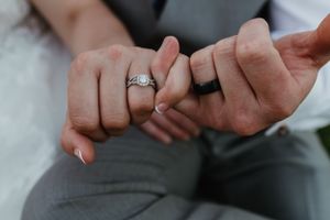 Close-up shot of newlyweds holding pinky fingers showing wedding rings.