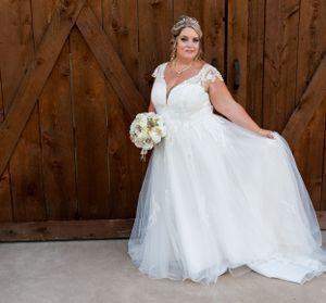 A bride in a flowing white dress poses with her bouquet against a wooden barn door.