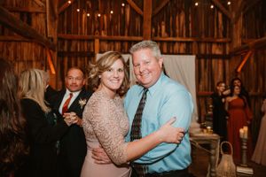 Guests dance at a rustic barn wedding reception with twinkling lights.