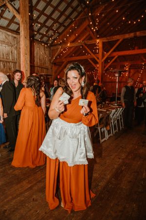 Person in orange dress celebrates at rustic barn wedding reception with string lights.
