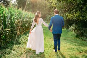 A wedding couple strolls hand in hand along a garden path during golden hour.