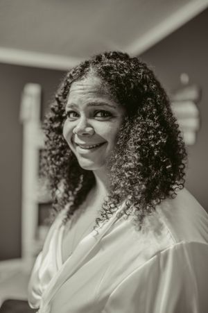 A radiant bride with natural curly hair smiles warmly in black and white photography.