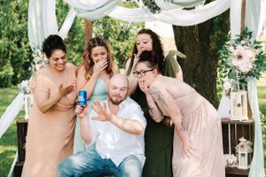 Fun candid moment of wedding party laughing together under decorated ceremony arch.