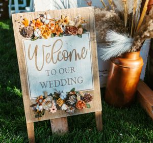 Wooden welcome sign decorated with dried flowers and copper accents for a rustic wedding.