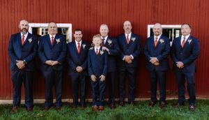 Group formal portrait against a red barn with matching navy suits and orange accents.
