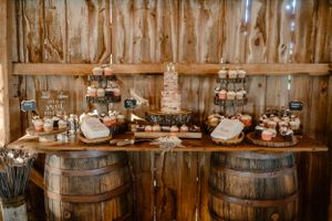 Rustic dessert bar setup with wooden barrel stands and multiple tiered displays in a barn setting.