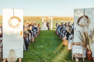 Outdoor wedding ceremony setup with rustic decor and dried flowers against a field backdrop.